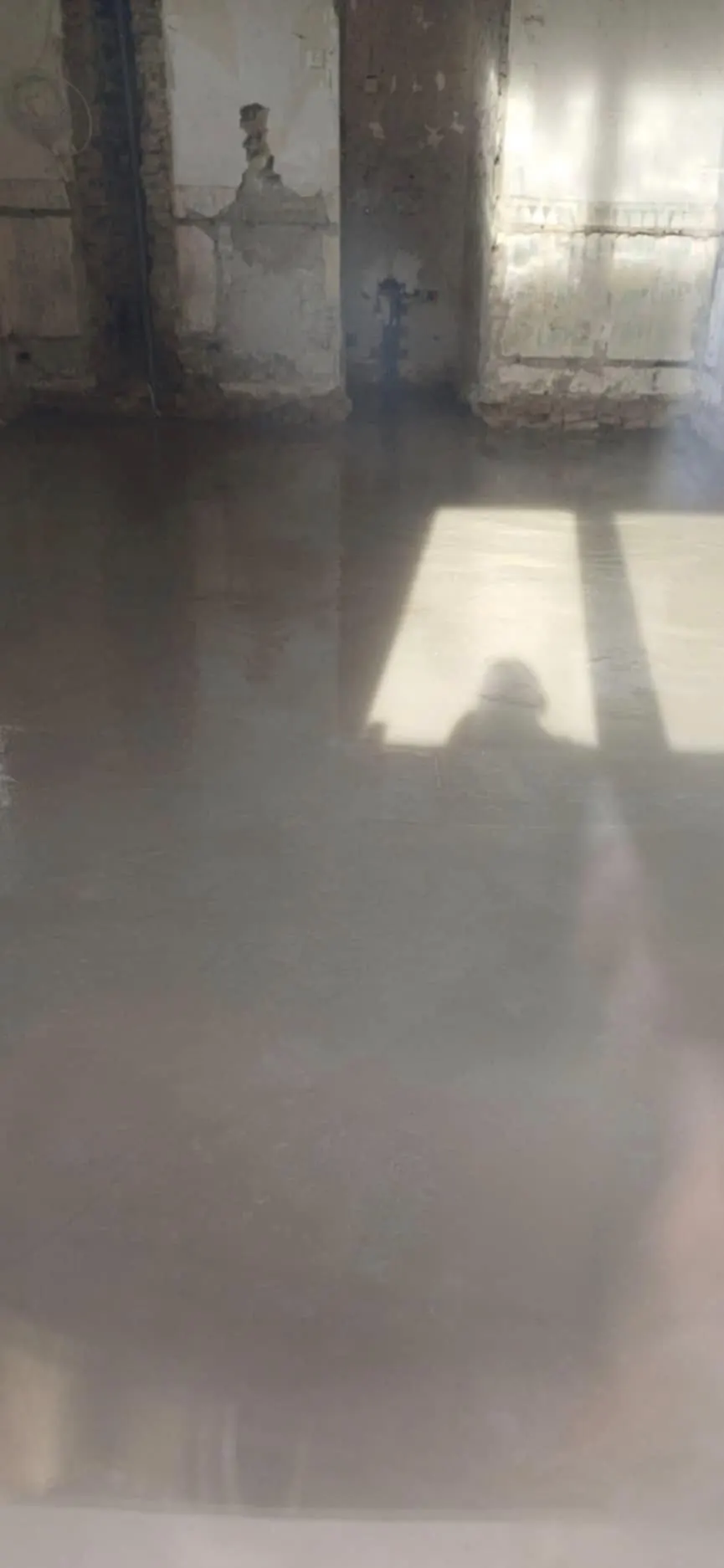 A Farkas-Konstrukt Kft. által végzett generálkivitelezés munkálatai Győrben. Az image egy frissen szigetelt és simított padlót mutat be, amelyen a napfény átsüt a nyitott ablakon, lágy árnyékokat vetve a felületre. A tiszta és sima felület a kiváló minőségű kivitelezést tükrözi, amely jellemző a cég munkáira.