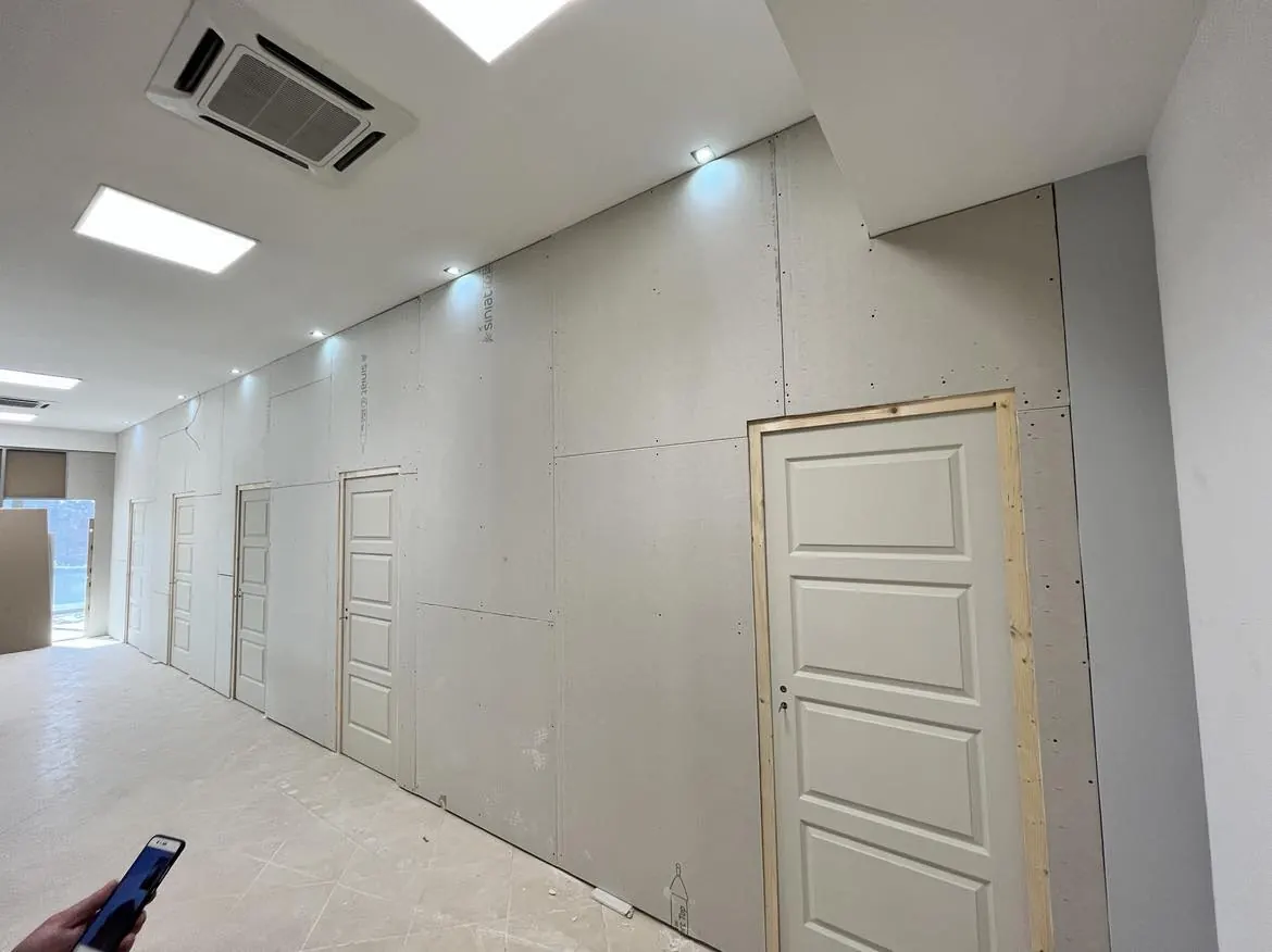 A képen egy frissen kialakított belső tér látható, ahol a falakat gipszkarton borítja, és több ajtókeret is előkészítés alatt áll. A világítás modern LED spotlámpákból áll, amelyek világítják meg a teret. A helyiség padlója még burkolásra vár, a munkálatokat a Farkas-Konstrukt Kft. végzi, amely Győr városában generálkivitelezéssel foglalkozik.