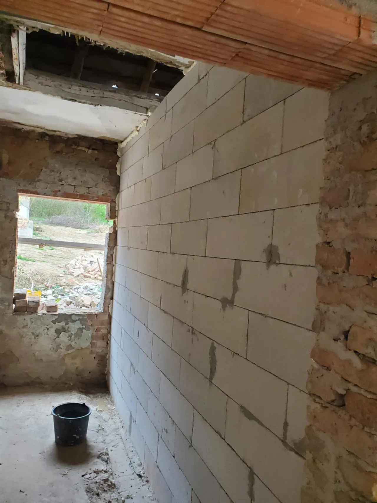 A képen egy építkezés látható, ahol a falazás folyamatban van. A falak fehér tégla blokkokból állnak, és a szoba belseje látható, ami Győr városában található. A nyitott ablakon keresztül a külső terület is látszik, ahol építési anyagok találhatók. A Farkas-Konstrukt Kft. generálkivitelezés szolgáltatásai segítik a modern építkezések megvalósítását.