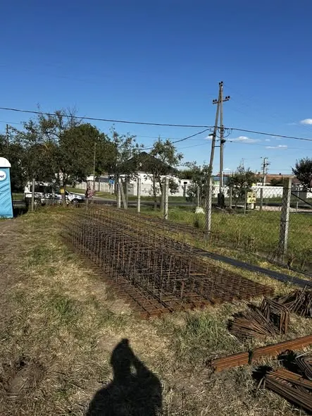 A képen a Farkas-Konstrukt Kft. generálkivitelezési munkálatai láthatók Győr városában. A háttérben látható fémrácsok és földmunka előkészületei, illetve a területen elhelyezett anyagok jól mutatják a kivitelezési folyamatot. A világos égbolt és a környező fák szép kontrasztot alkotnak a munkaterületen.