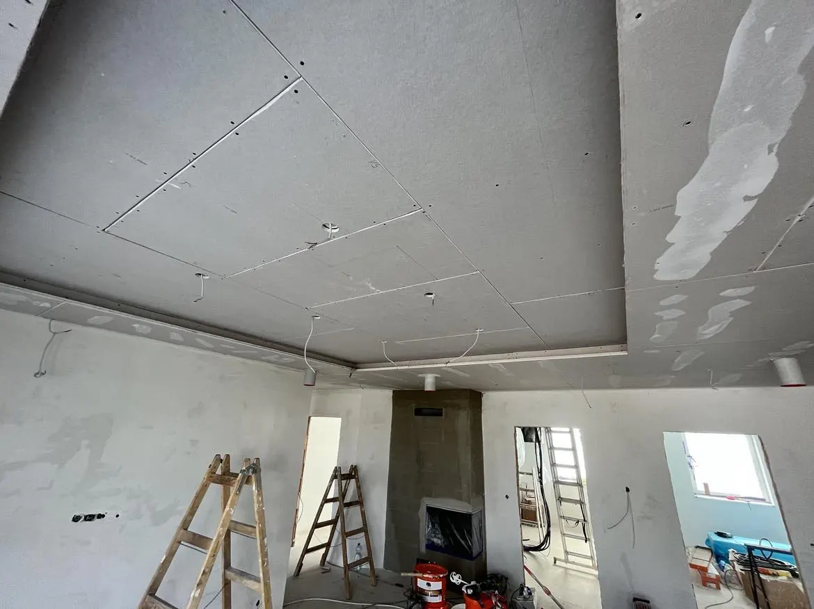 A képen egy frissen felújított belső tér látható, ahol a mennyezet gipszkarton borítással készül. A falak fehérre festettek, és a padlón létrák, valamint építőipari eszközök találhatók. A képen látható munkálatok a Farkas-Konstrukt Kft. generálkivitelezési szolgáltatásait tükrözik Győr városában, ahol a modern építkezés és felújítás folyamatban van.