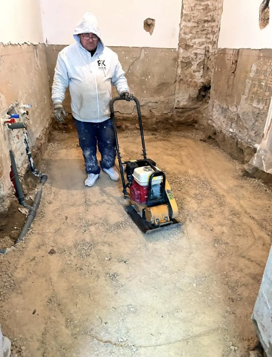 A képen egy Farkas-Konstrukt Kft. munkatársa látható, amint földmunkát végez egy épület belső terében Győr városában. Az aljzat előkészítése érdekében egy döngölőgépet használ, miközben a falak repedezettek és a padló még nyers állapotban van. A munka minőségi generálkivitelezés részeként zajlik, tükrözve a cég szakértelmét és elkötelezettségét.