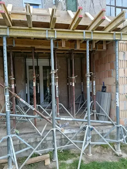 A képen egy építkezési terület látható, ahol állványzat és támrendszer található, amely a falak támogatására szolgál. Az állványok megfelelően rögzítve vannak, a háttérben egy épület részletei látszanak. A kép Győr városában készült, ahol a Farkas-Konstrukt Kft. generálkivitelezési munkálatai folynak. Az építkezés biztonságos kivitelezése érdekében a megfelelő eszközök és módszerek alkalmazása figyelhető meg.