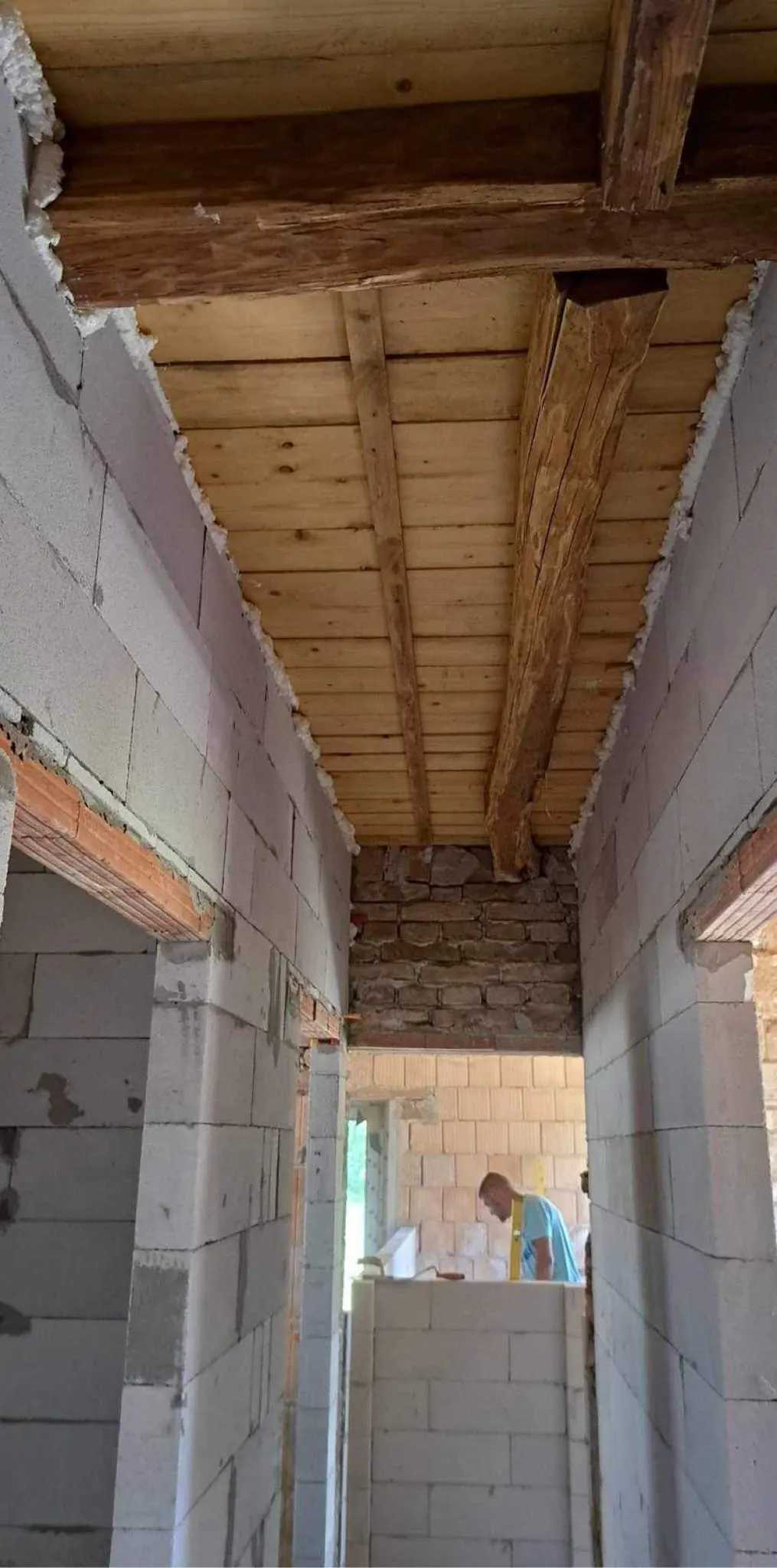 A képen egy építkezés látható, ahol a Farkas-Konstrukt Kft. generálkivitelezésével készül egy belső tér Győr városában. A falak még csak részben készültek, láthatóak a betonblokk elemek és a fa gerendák, amelyek a mennyezetet tartják. Az építkezés folyamata jól tükrözi a modern építési technikákat és a precíz munkát, amit a cég képvisel.