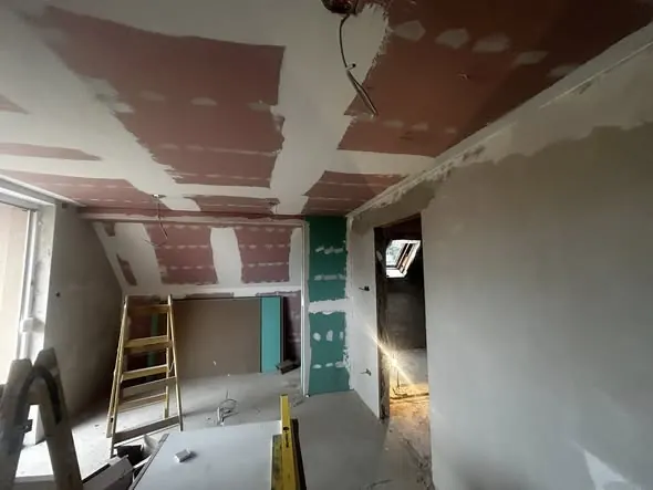 A képen egy felújítás alatt álló helyiség látható, ahol a falak és a mennyezet gipszkartonozása zajlik. A háttérben lévő létra és a különböző építkezési anyagok arra utalnak, hogy a munka folyamatban van. A Győr városában működő Farkas-Konstrukt Kft. szakértői a generálkivitelezés terén nyújtanak professzionális szolgáltatásokat.