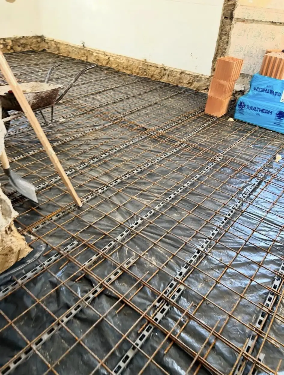 A képen a Farkas-Konstrukt Kft. betonozási munkálatai láthatók Győr városában. A területen acélszerkezet és fólia található, amely a betonozás előkészítését szolgálja. Az eszközök, mint például a talicska és a lapát, is jól láthatóak, amelyek a generálkivitelezés folyamatához szükségesek. A háttérben a falak és a földszinti alapozás részletei figyelhetők meg.