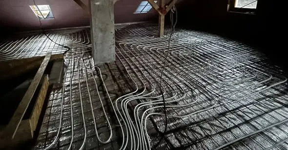 A képen egy építkezés látható, ahol a padlófűtés csövei gondosan elhelyezve futnak a betonpadlón. A munkálatok Győr városában zajlanak, és a Farkas-Konstrukt Kft. Generálkivitelezés tevékenységét tükrözik. Az épület belső terében jól láthatók a fűtéshez szükséges csövek, amelyek a projekt precíz tervezését és kivitelezését jelzik.