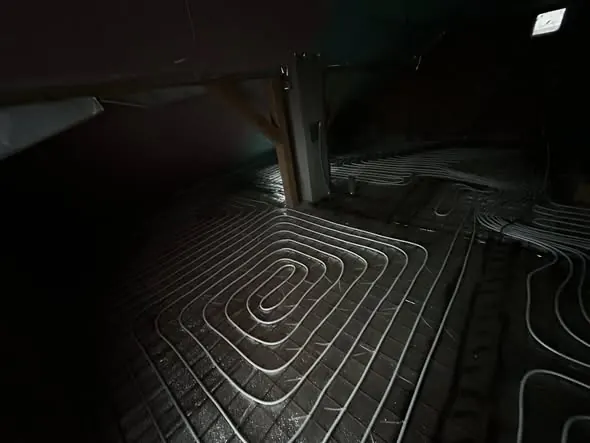 A képen egy épület padlóján elhelyezett fűtőcsövek láthatók, amelyek precíz elrendezésük révén biztosítják a hatékony fűtést. A csövek szakszerű telepítése a Farkas-Konstrukt Kft. generálkivitelezési szolgáltatásának része, amely Győr városában érhető el. A sötét háttér kiemeli a csövek fényes vonalait, ami modern és jól megtervezett kivitelezést sugall.