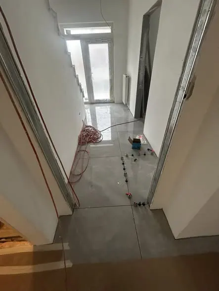 A képen egy családi ház belső terének kivitelezése látható, ahol a padlóburkolat már elkészült, és a falak is készülnek. A Győr városában működő Farkas-Konstrukt Kft. Generálkivitelezés szolgáltatása keretében zajlik a munka. Az építkezés során a világítás és az elektromos vezetékek telepítése is folyamatban van, ami a modern otthonok kialakításához szükséges.