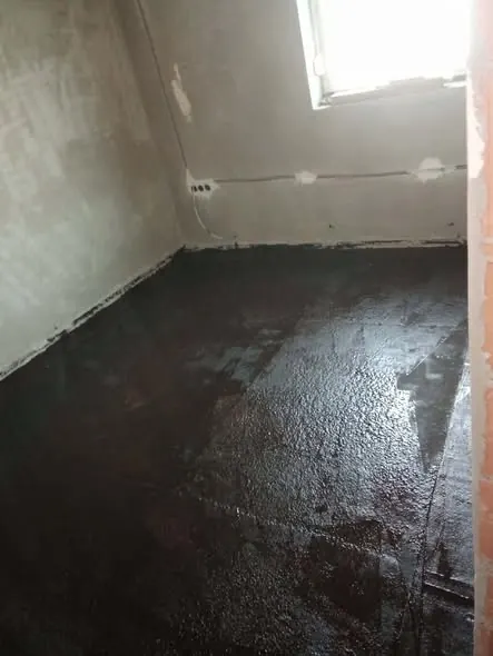 A képen egy frissen kiegyenlített betonpadló látható, amely éppen a generálkivitelezés fázisában van. A falak még érintetlenek, a szoba világos ablakán átsüt a napfény, ami kiemeli a padló sima felületét. Ez a munka a Farkas-Konstrukt Kft. Körmend városában zajlik, ahol a cég szakértelme a generálkivitelezés terén érvényesül.