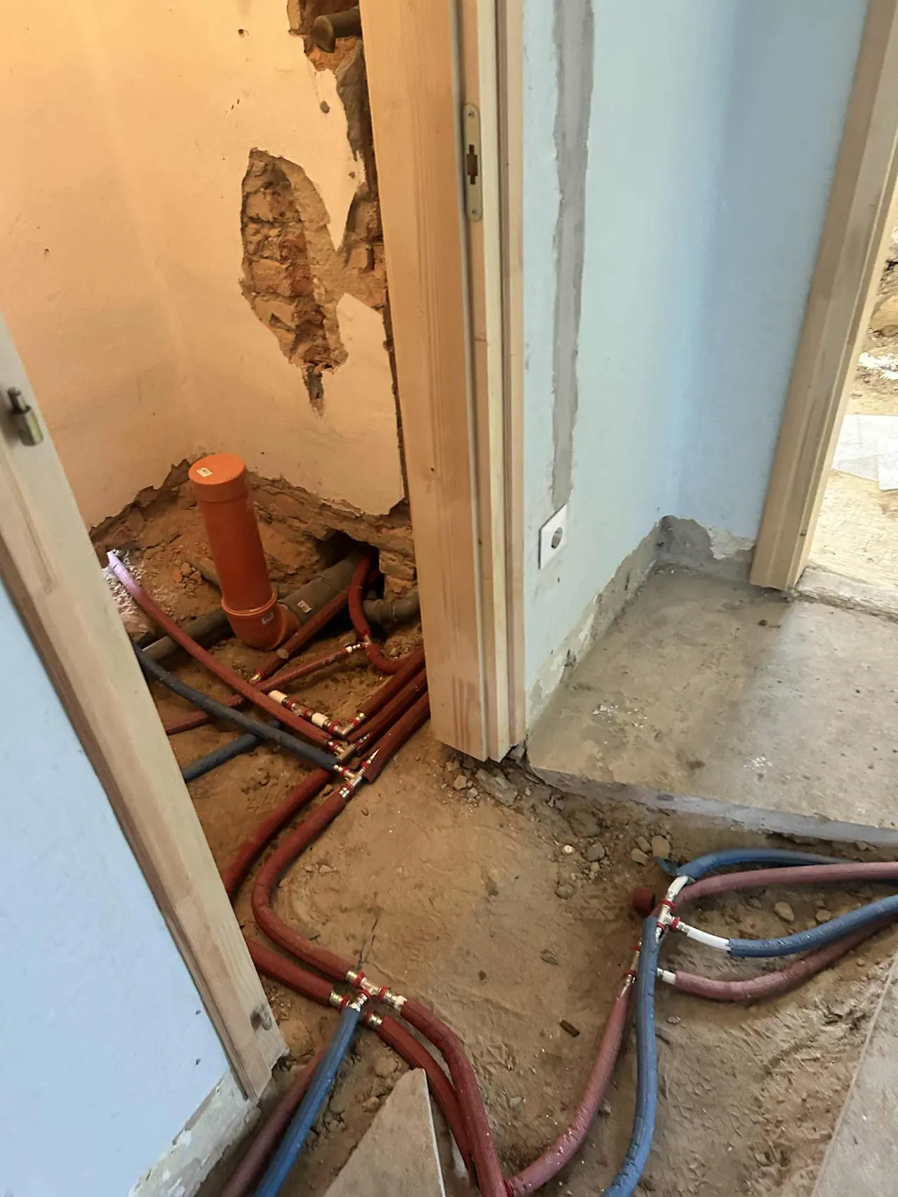 A képen egy építkezési terület látható Győr városában, ahol a Farkas-Konstrukt Kft. generálkivitelezési munkálatokat végez. Az injektálási folyamat részeként különböző színű csövek láthatók a földön, amelyek az épület falain keresztül futnak. A falon már láthatók a felújítás nyomai, ahogy a burkolat is hiányzik. Az építkezési környezet jól tükrözi a generálkivitelezés dinamikus jellegét.