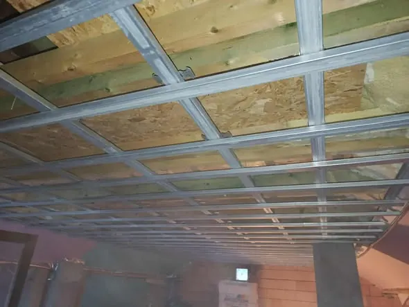 A képen egy építkezés látható, ahol az acélszerkezet és az OSB lapok már a helyükre kerültek. Az építkezés Győrben zajlik, ahol a Farkas-Konstrukt Kft. által végzett generálkivitelezés folyamatát figyelhetjük meg. A világítás halványan világítja meg a munkaterületet, ami a jövőbeli belső tér kialakítását segíti elő.