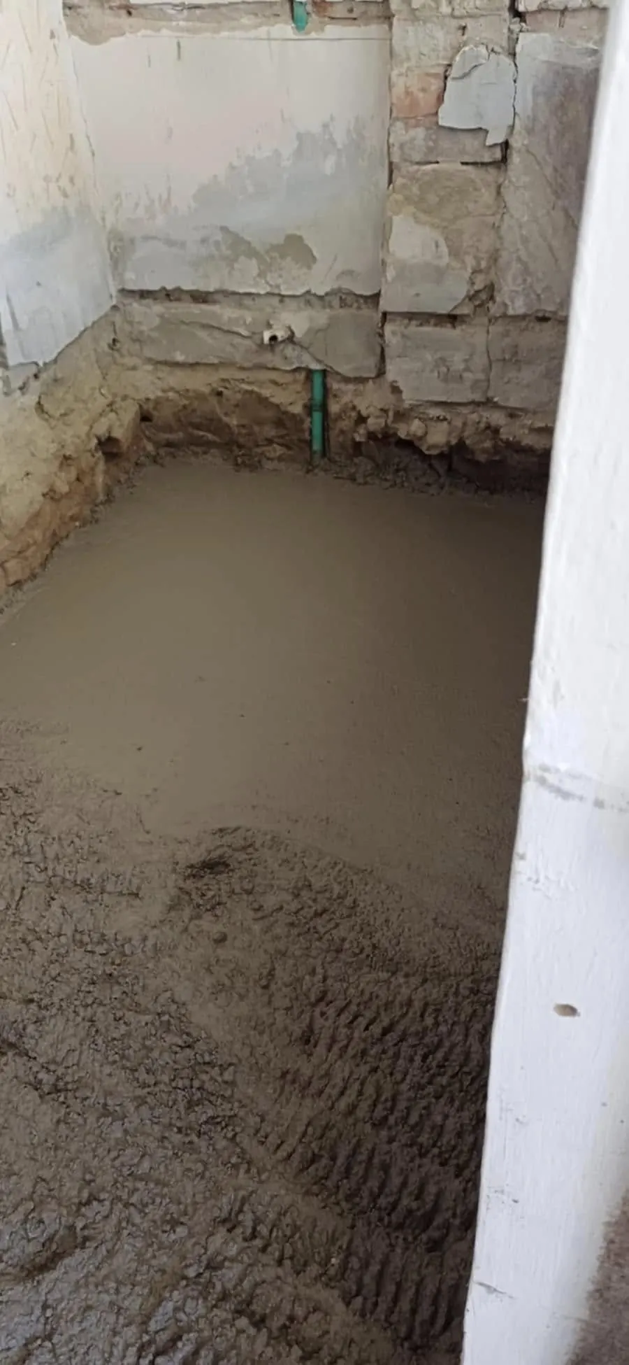 A képen egy frissen betonozott terület látható, amely Győr városában készült a Farkas-Konstrukt Kft. generálkivitelezési szolgáltatása keretében. A beton sima felülete és a falnál látható zöld cső azt mutatja, hogy a munka precízen és szakszerűen zajlott. A környezetben látható a falak textúrája, amelyek a felújítás előtti állapotot tükrözik.