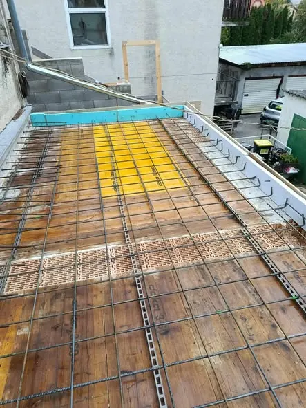 A képen egy betonozásra előkészített terület látható, ahol a Farkas-Konstrukt Kft. generálkivitelezés szolgáltatása zajlik Győr városában. A betonozás előtt az acélgerendák és a fémhálók precíz elrendezése látható, amelyek biztosítják a stabilitást és tartósságot. A háttérben egy épület falai és egy nyitott terület is megfigyelhető, ami a munka folyamatát jelzi.