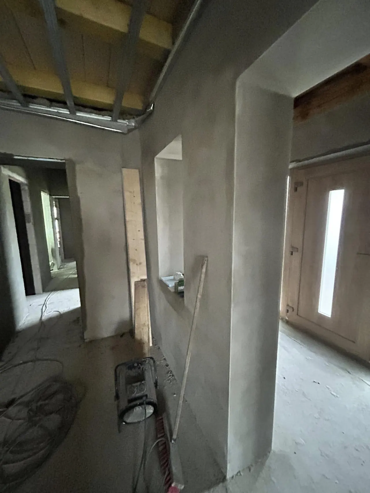 A képen egy frissen épített belső tér látható, mely Bük városában található. A falak simára vakoltak, a mennyezeten látható a fa tartószerkezet. Az ajtók modern stílusúak, és a padlón építkezéshez szükséges eszközök találhatóak. A Farkas-Konstrukt Kft. Generálkivitelezés tevékenysége nyomán készült ez a tér, amely a jövőbeli lakások alapját képezi.