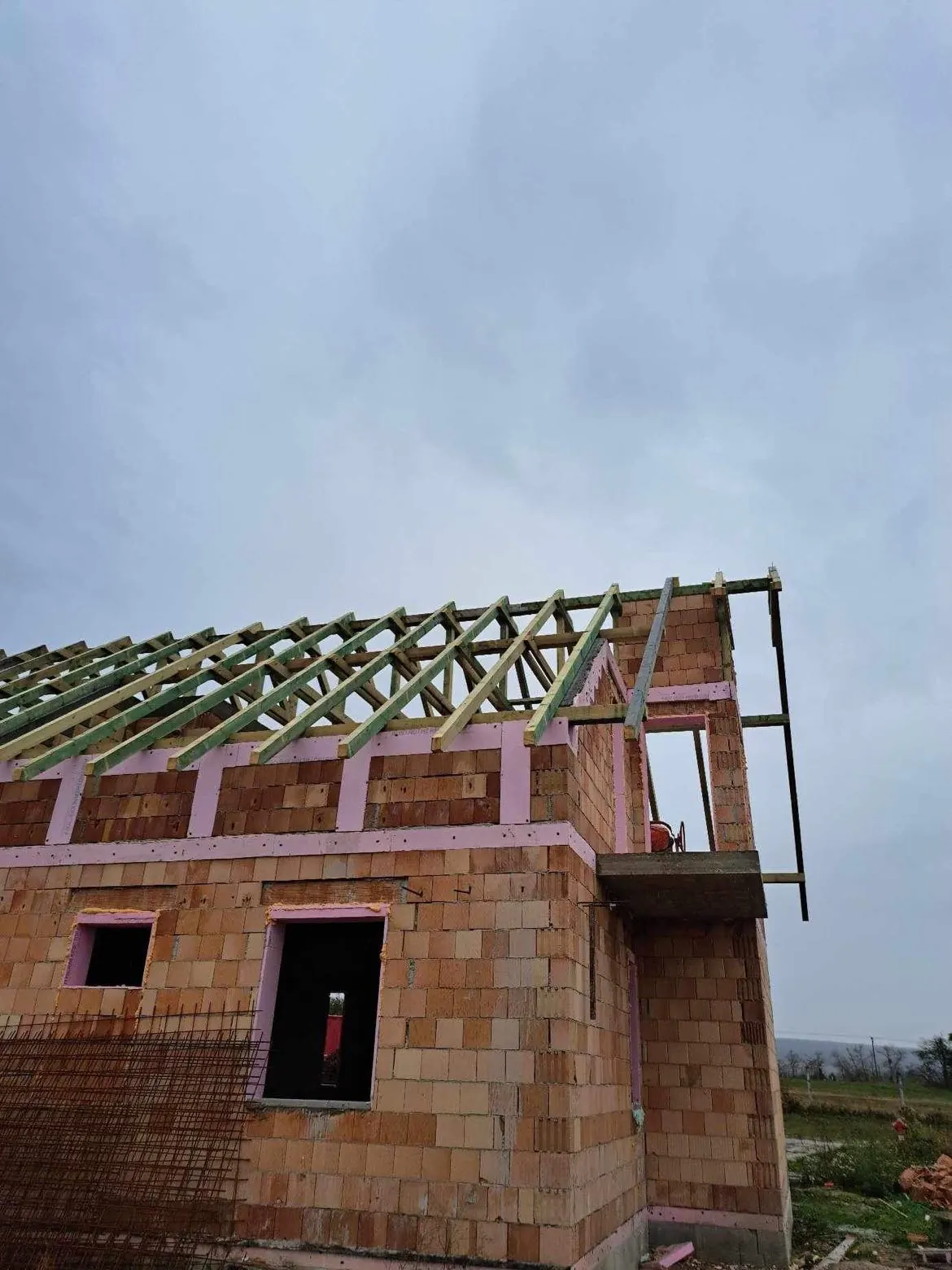 Győr városában, a Farkas-Konstrukt Kft. generálkivitelezés projektjén egy épület tetőszerkezete látható, amelynek vázát már elkészítették. A falak téglából épülnek, és szigetelőanyagokkal vannak ellátva. Az építkezés során a munka pontosan halad, a szürke égbolt pedig a téli időszakot idézi.