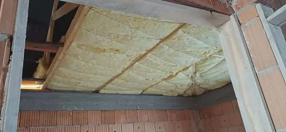 A képen a Farkas-Konstrukt Kft. hőszigetelési munkálatai láthatók, amelyek Győr területén zajlanak. A falak között hőszigetelő anyag, sárga színű szigetelés található, amely a mennyezet alatt helyezkedik el. A tégla falak és a látható szerkezetek, mint például a fagerendák, a generálkivitelezés folyamatát tükrözik, amely biztosítja a megfelelő hőszigetelést a közelgő építkezési projektekhez.