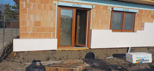 Az új építés alatt álló ház Győrben, amely a Farkas-Konstrukt Kft. generálkivitelezésének részeként készült. A képen látható a ház homlokzata, a téglák és az új ablakkeretek, valamint a frissen készült alapozás. A munka során a cég a legjobb minőségű anyagokat használja, hogy a végeredmény tartós és esztétikus legyen.