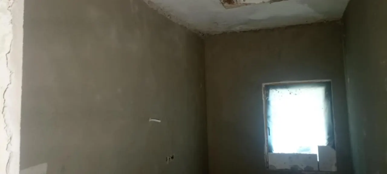 A képen egy frissen vakolt fal látható, amely a Farkas-Konstrukt Kft. generálkivitelezési munkálatainak része Győr városában. A szoba sarkában egy ablak található, amelyen át a természetes fény bejut. A falak sima felülete a burkolás előkészítését jelzi, ami a cég burkoló szolgáltatásainak fontos része.