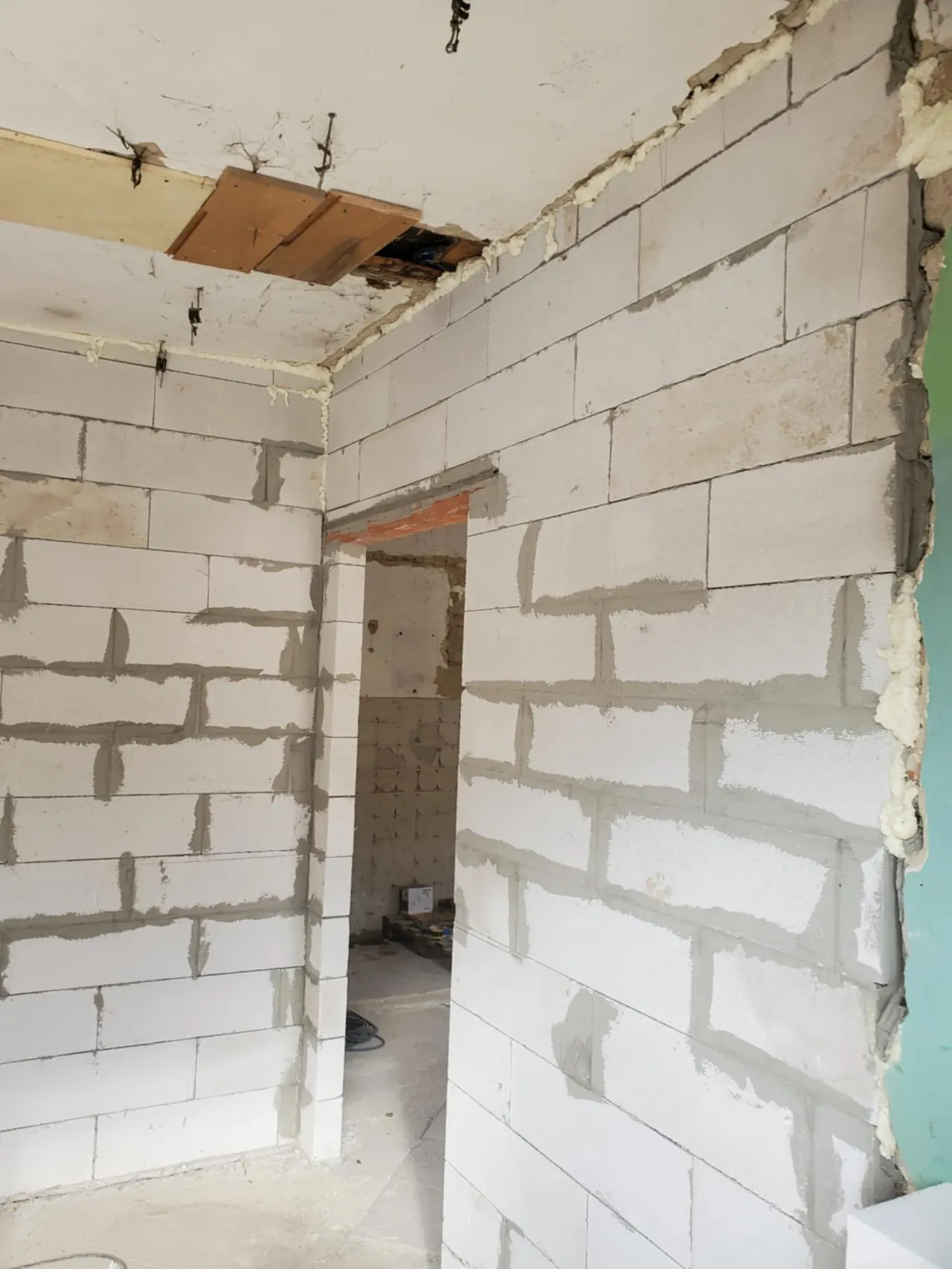 A képen egy építkezési helyszín látható, ahol a falakat még nem fejezték be. A falak blokkokból készülnek, és azokon látható a friss habarcs. A háttérben egy nyílás található, amely egy másik helyiségbe vezet. A képen jól érzékelhető a munka előrehaladása, amely a Farkas-Konstrukt Kft. által végzett generálkivitelezés során készült Győr városában.