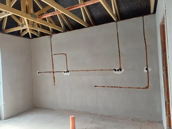 A képen egy frissen elkészült belső tér látható, ahol a falak simára vakoltak, és a villanyvezetékek előkészítve a következő lépésekhez. A tetőszerkezet fagerendái jól láthatók, a padló még nem burkolt. A kép Csornán készült, a Farkas-Konstrukt Kft. generálkivitelezési munkálatainak részeként.