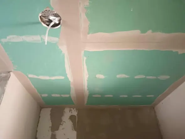 A képen egy frissen elkészült gipszkarton fal látható, amely zöld alapozóval van kezelve, készen a további festéshez vagy burkoláshoz. A falon látható a világítótest számára készített kábel, amely a generálkivitelezés folyamatát tükrözi. A kép Tata városában készült, ahol a Farkas-Konstrukt Kft. szakértelmével a legjobb minőségű kivitelezési munkákat végzi.