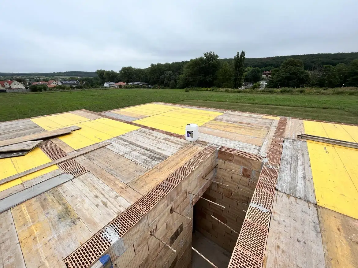 Győr városában a Farkas-Konstrukt Kft. generálkivitelezési projektje látható, ahol egy építkezés előkészületei zajlanak. Az építkezési területen a falazás és az alapozás munkálatai folyamatban vannak, a fa panelok és téglaanyagok rendezett elhelyezése jól látható. A zöld terület és a háttérben látható házak növelik a projekt környezetének megjelenését.