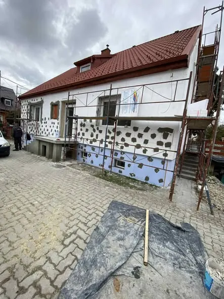 Új építkezés folyamata látható Győr városában, ahol a Farkas-Konstrukt Kft. generálkivitelezési szolgáltatásaival kulcsrakész kivitelezést végez. A ház homlokzatán éppen befejezés előtt álló szigetelőmunka látható, a falon pedig a festés előkészítése zajlik. A területen állványzat és építőanyagok találhatók, amelyek a kivitelezés folyamatát segítik.