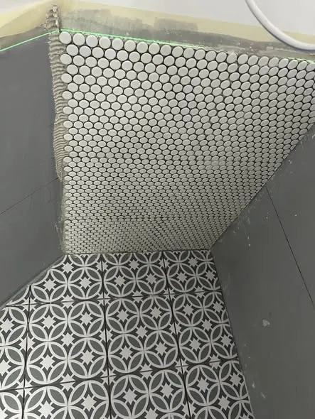 A képen egy felújítás alatt álló fürdőszoba látható, ahol a falon kör alakú mozaikcsempék vannak elhelyezve, míg a padló díszes, geometrikus mintázatú járólappal van burkolva. A Farkas-Konstrukt Kft. Generálkivitelezés szolgáltatásának részeként készült munka Győr városában, amely a modern és esztétikus fürdőszobák iránti igényeket szolgálja ki.