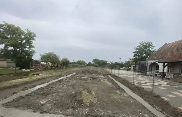 A képen egy frissen elkészült generálkivitelezési terület látható Győrben, ahol az alapozási munkálatok zajlanak. A földkitermelés után a terület síkba lett hozva, körben kerítéssel elkerítve. A háttérben fák és házak láthatók, amelyek a környező lakóövezetet jelzik. A Farkas-Konstrukt Kft. szakszerűen végzi a kivitelezést, biztosítva a magas minőséget.