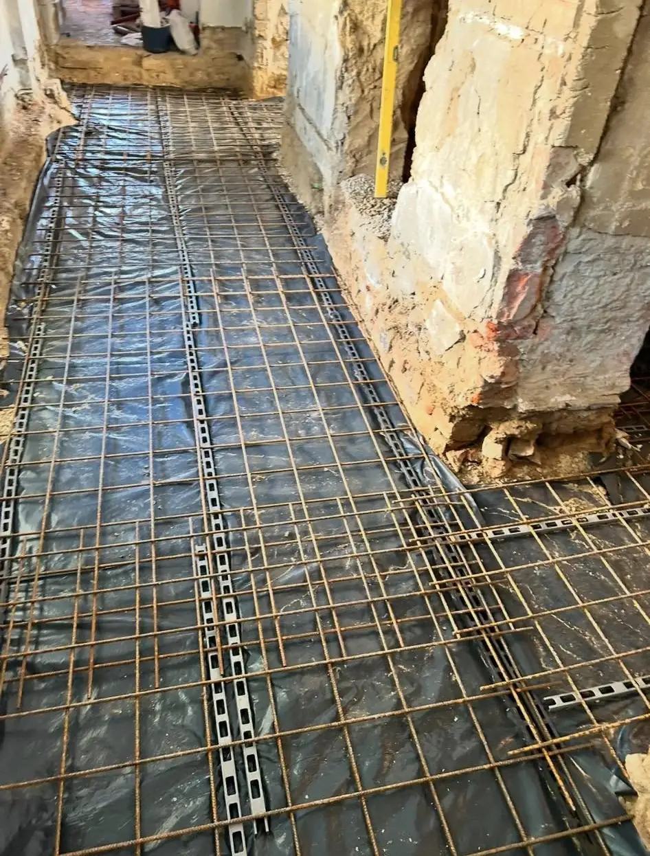 A képen a Farkas-Konstrukt Kft. által végzett betonozás látható, amely Győr városában zajlik. A felvételen egy felújítás alatt álló helyiség látható, ahol az aljzat előkészítése folyik. A betonozás előtt elhelyezett vasalás jól látható, amely a tartósságot és stabilitást szolgálja. A falak részben láthatók, amelyek a munkálatok előrehaladását tükrözik a generálkivitelezés folyamatában.