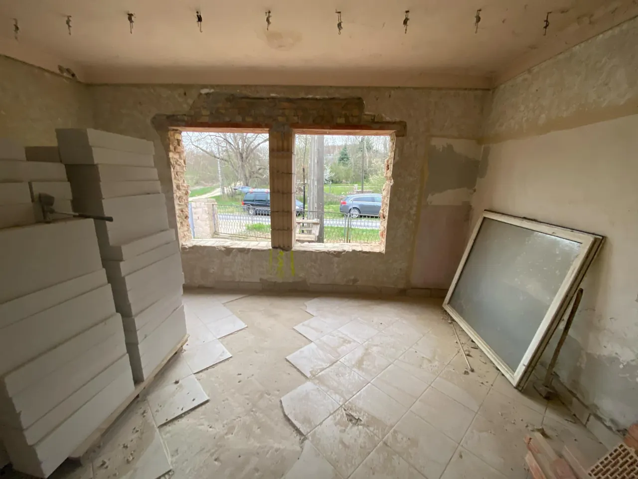 A képen egy még befejezetlen generálkivitelezési projekt látható Sopronban. A helyiség falai részben le vannak bontva, a padlón félig lerakott csempe található, míg az ablakok előtt frissen felújított keretek láthatók. Az ablakokból a külső terület látszik, ahol autók parkolnak. A munkaterület rendezett, de a kivitelezés folyamatban van, ami a Farkas-Konstrukt Kft. szakértelmét tükrözi.