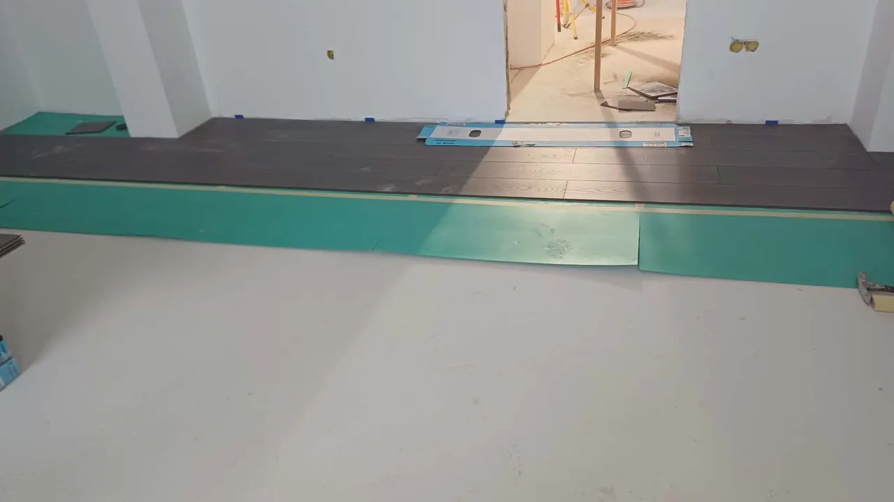 A képen a Farkas-Konstrukt Kft. burkolási munkálatai láthatók Győrben, ahol egy frissen burkolt padló részletei látszanak. A fekete és zöld burkolóanyagok szépen illeszkednek egymáshoz, a háttérben pedig a készülő helyiség kontúrjai és eszközök fedezhetők fel, amelyek a generálkivitelezés során használatosak.