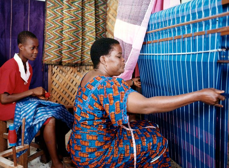 An artisan from the Igbo-Ndoki people in Nigeria weaving traditional Akwete cloth on a vertical, double-heddle loom, featuring wide, complex geometric patterns woven directly into the fabric structure. An artisan from the Igbo-Ndoki people in Nigeria weaving traditional Akwete cloth on a vertical, double-heddle loom, featuring wide, complex geometric patterns woven directly into the fabric structure.