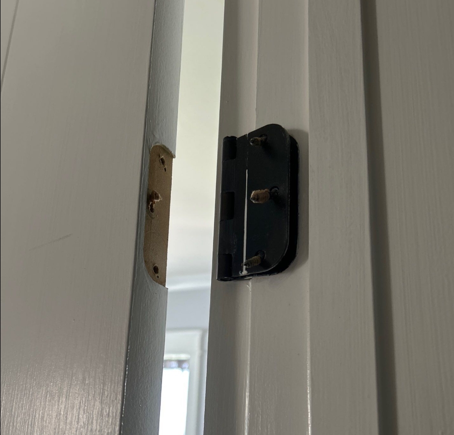 Close-up of a damaged interior door hinge with loose screws and the hinge plate pulled away from the doorframe before repair