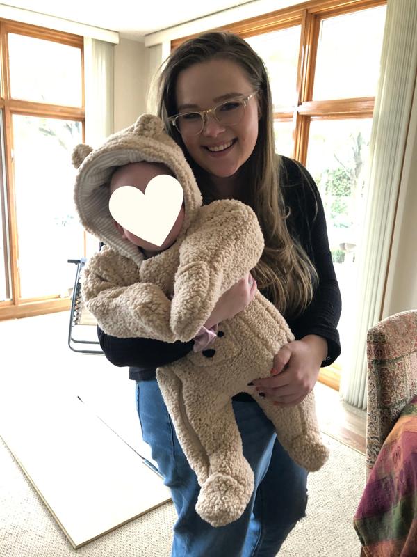 Rachel smiling and holding her baby son in a fuzzy bear outfit