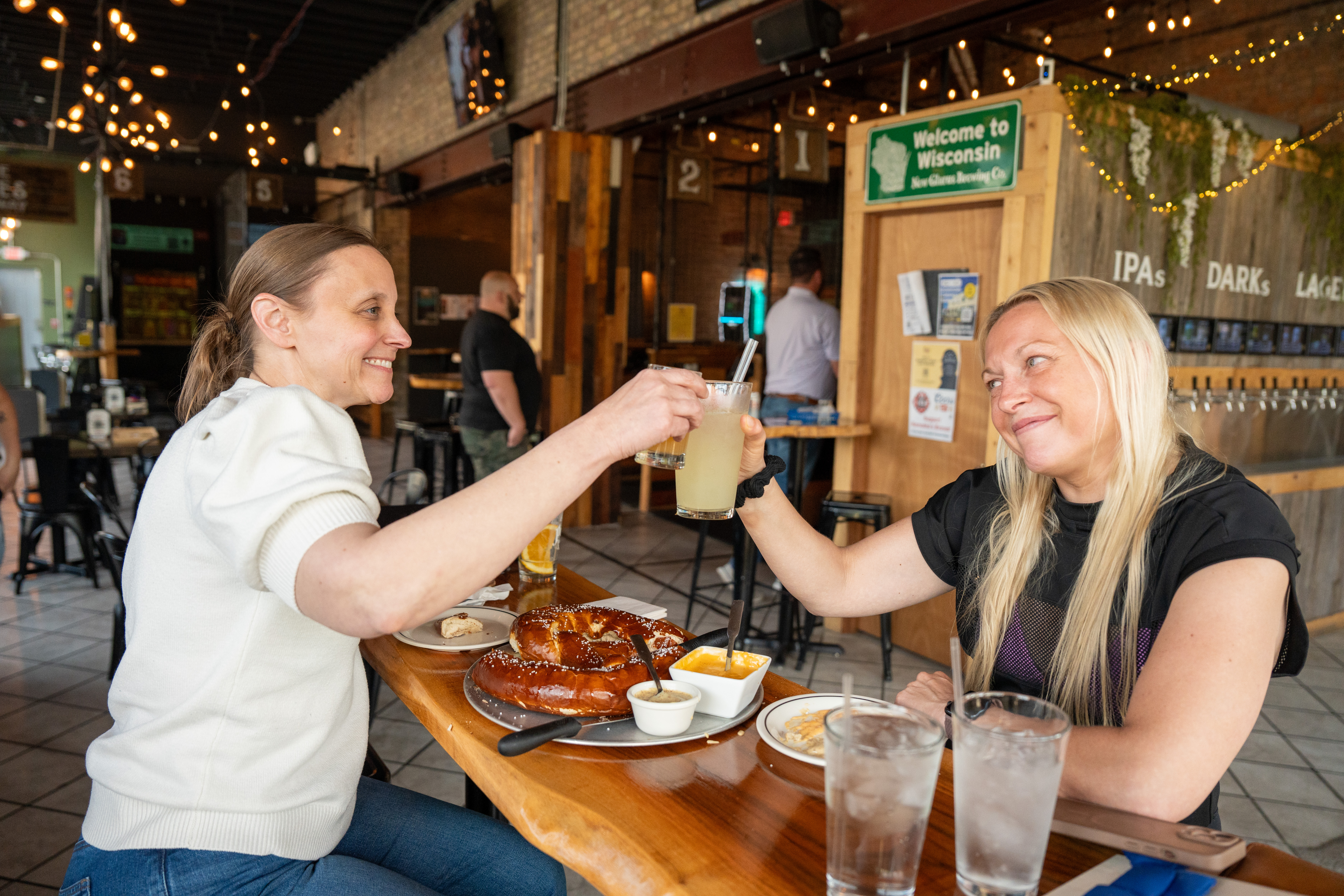 Friends toasting drinks with a Milwaukee pretzel on the table at Hold My Beer Kenosha