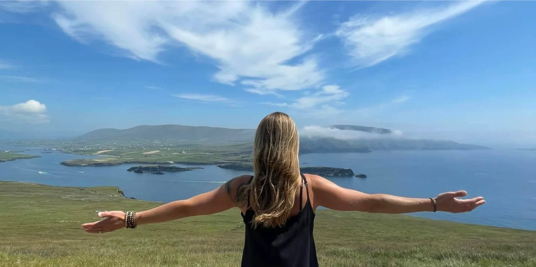 Katharina standing with open arms overlooking the Irish coastal landscape.