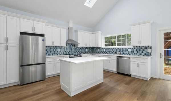Modern ADU kitchen with white shaker cabinets, center island, stainless steel appliances, and blue backsplash tile.