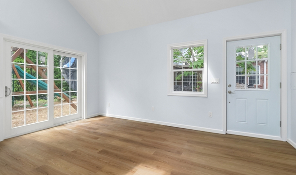 Open-concept ADU living room featuring light blue walls, wood flooring, sliding glass door, and blue front door.