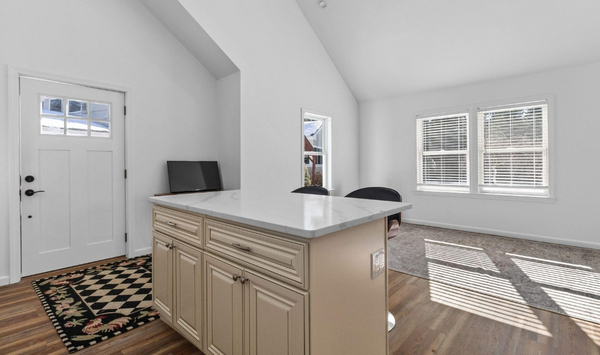 Small ADU kitchen and living area with a marble-look island, light cabinetry, wood flooring, and large windows. Small ADU kitchen and living area with a marble-look island, light cabinetry, wood flooring, and large windows.