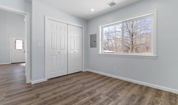 Bright ADU bedroom in Connecticut with large window, closet storage, and wood-look flooring