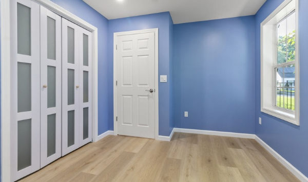 Blue-walled room with wood flooring, white closet doors, and a window, suitable for an ADU home office layout.