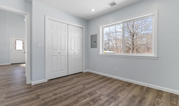 Bright empty room with gray walls, large window, closet storage, and wood-look flooring for a potential ADU home office.