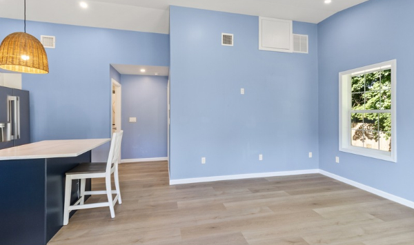 Open residential interior with blue walls, kitchen island, wood-look flooring, and natural light, illustrating ADU home office finishes.  