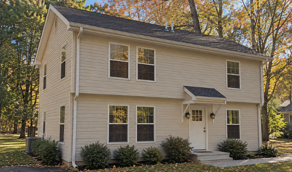 Angled exterior view of a custom two-story ADU with two levels of windows, beige siding, and a covered entry.