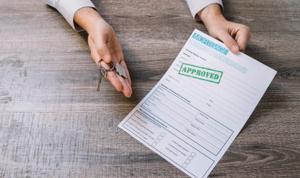 Person holding an approved mortgage application and house keys, illustrating home financing options for ADU construction.
