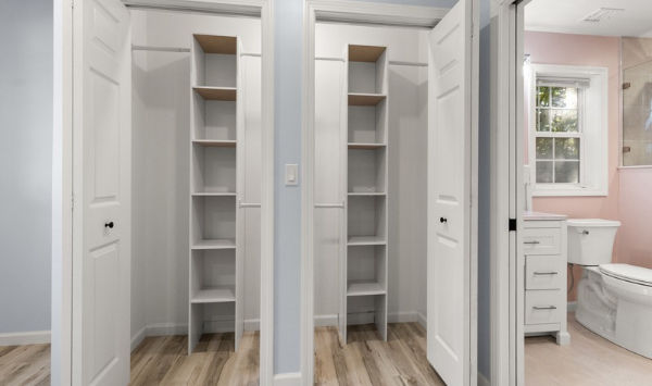 Two built-in storage closets with white shelving beside a bathroom in a residential interior.