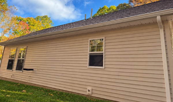Side exterior of a beige-sided residential building with windows, roofline, and autumn trees.