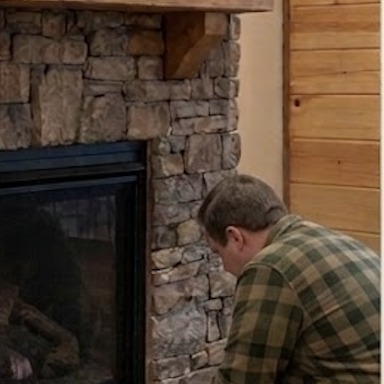 A Lodge Masters technician working on a stone fireplace hearth in a cabin living room